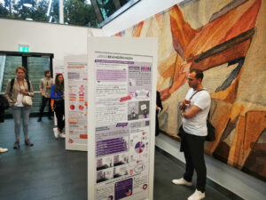 Personen betrachten die Infosäulen der Wanderausstellung Pfad der Vielfalt, ein Kunstwerk im Hintergrund