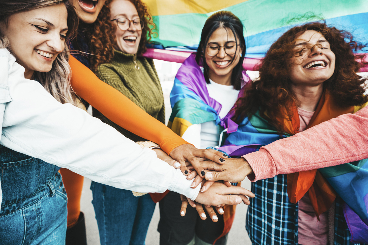 Group of people stacking hands outside with rainbow flag.